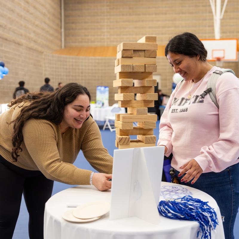 Two students playing jenga with a tower of wood blocks