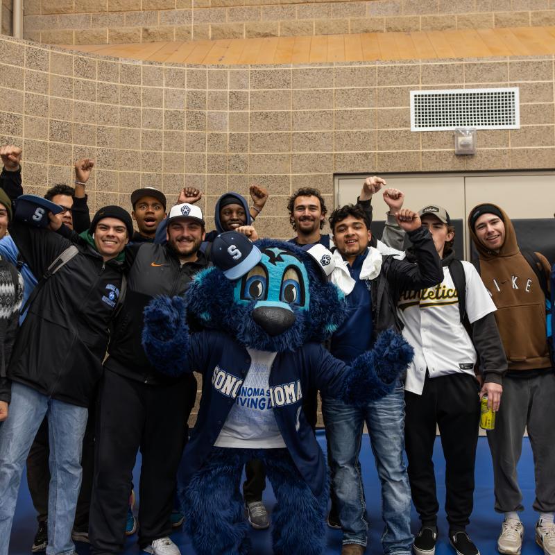 Group of students from club baseball cheering with hands in the air and lobo standing in the middle of the group